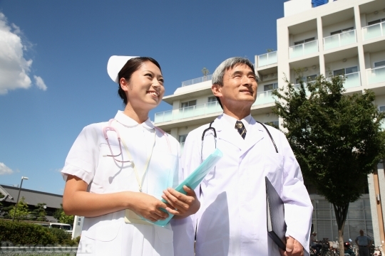 Devostock MALE DOCTOR AND FEMALE NURSE STANDING IN FRONT OF HOSPITAL