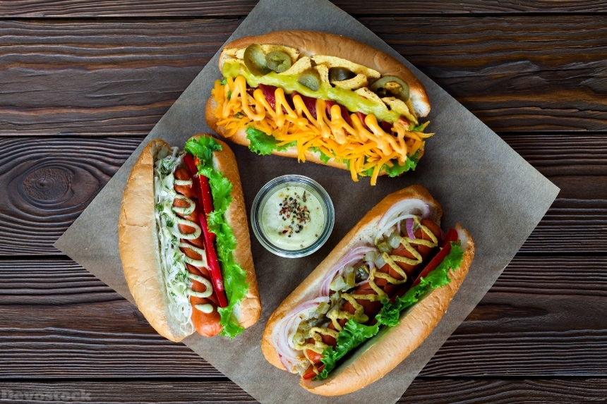 Devostock Assorted three hot dogs with sauce and salad on a wooden backgro