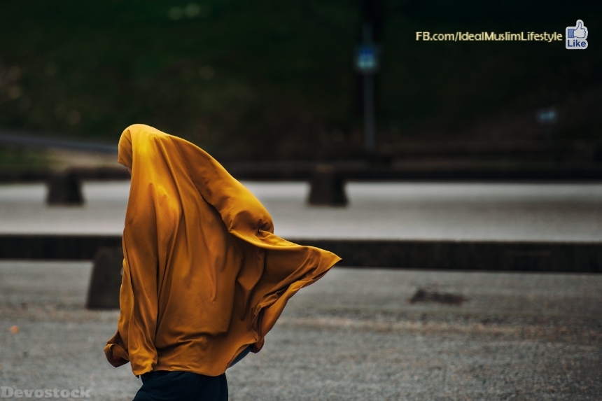 Devostock Muslim woman with long veil walking away 