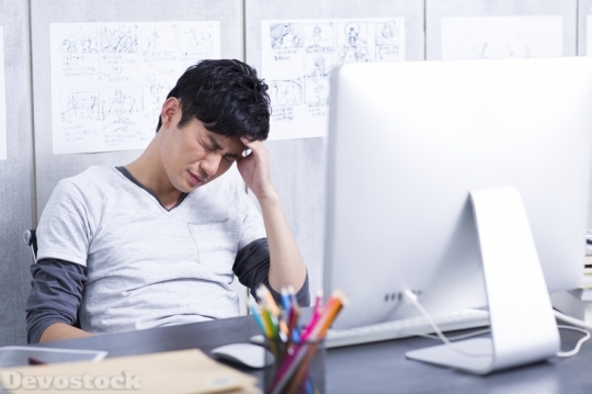 Devostock Young man having a headache in the office